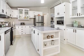 Eine moderne Küche mit weißen Schränken, einem Edelstahlkühlschrank, einer Mikrowelle und einer Kaffeemaschine.