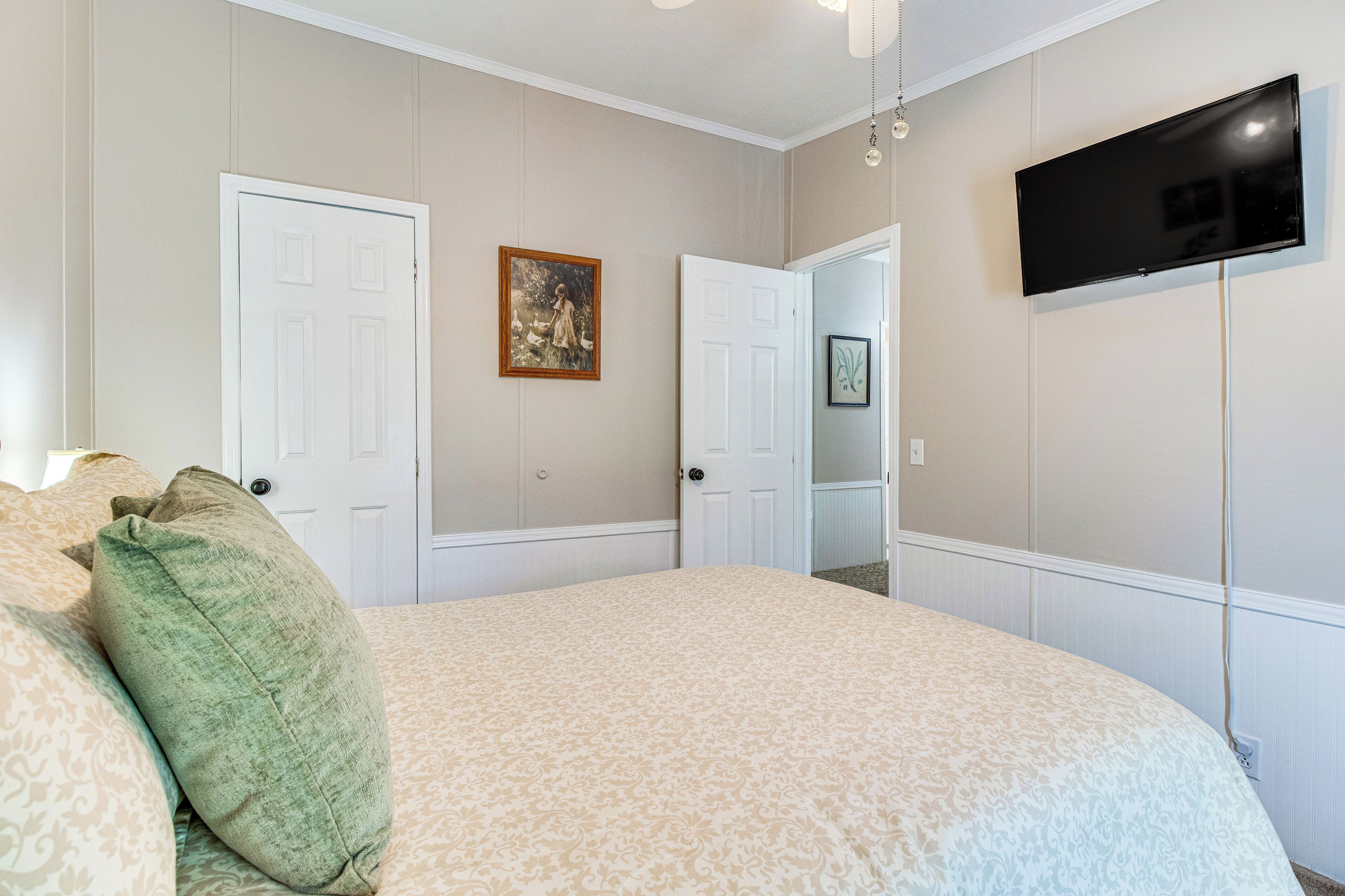 Un dormitorio con una cama, un televisor en la pared y dos puertas.