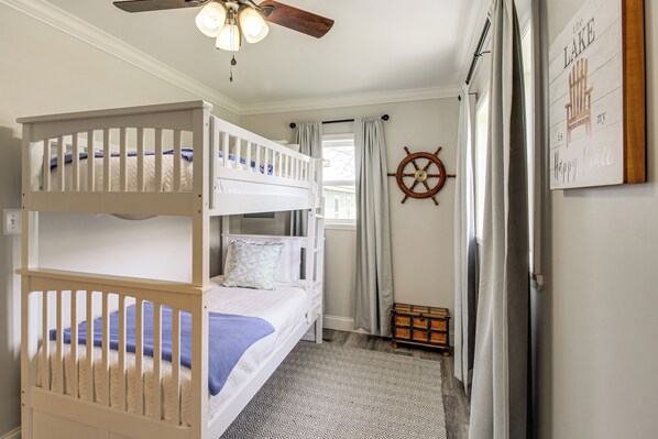Une chambre avec un lit superposé, un ventilateur de plafond, un gouvernail de bateau et un panneau décoratif encadré.