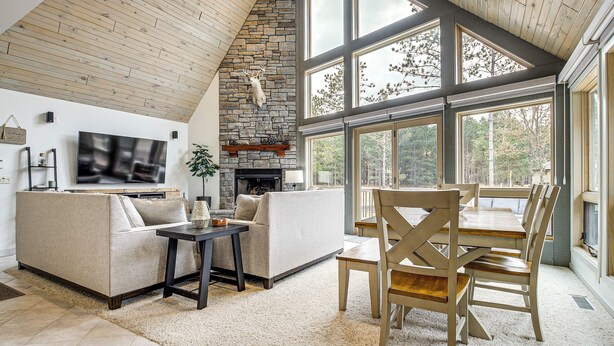 A spacious living room with a stone fireplace, a large TV, and a dining area with wooden chairs and a table.