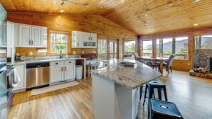 A spacious kitchen with wooden ceiling, white cabinets, and a large island with stools.