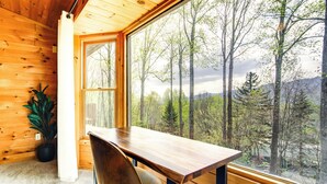 A wooden interior with a large window, a wooden table, and a chair.