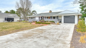 Une maison de plain-pied avec un garage, une allée et un petit jardin devant, agrémenté d’aménagements paysagers.