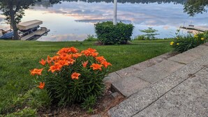 Une vue sur le lac avec un quai, une zone herbeuse parsemée de fleurs orange et un ciel dégagé.