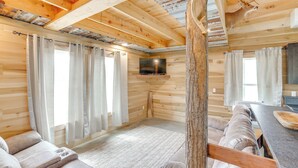 A cozy cabin interior with a wooden ceiling, a sofa, a dining table, and a mounted television.