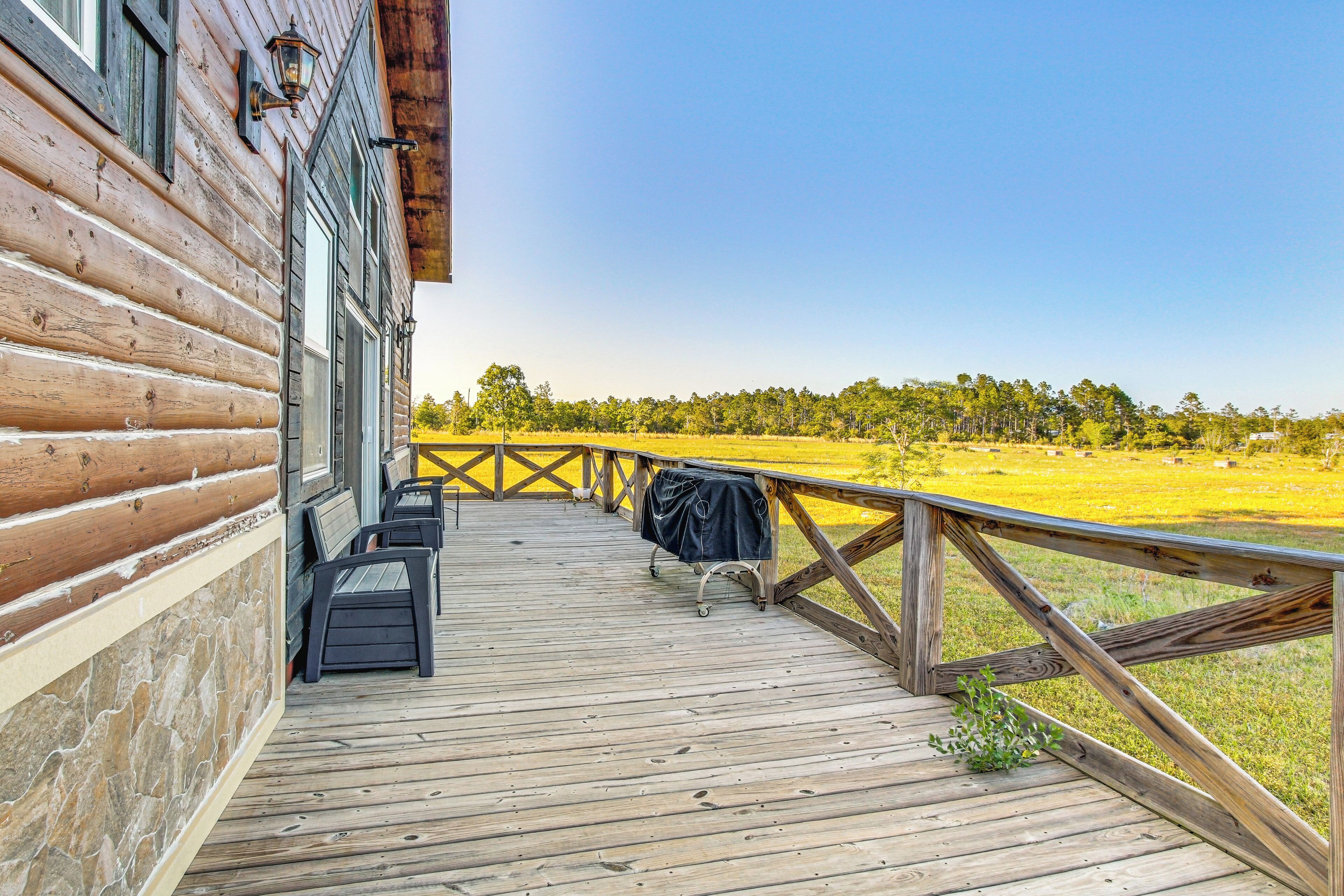 A wooden deck with outdoor seating, a barbecue grill, and a view of a grassy field.