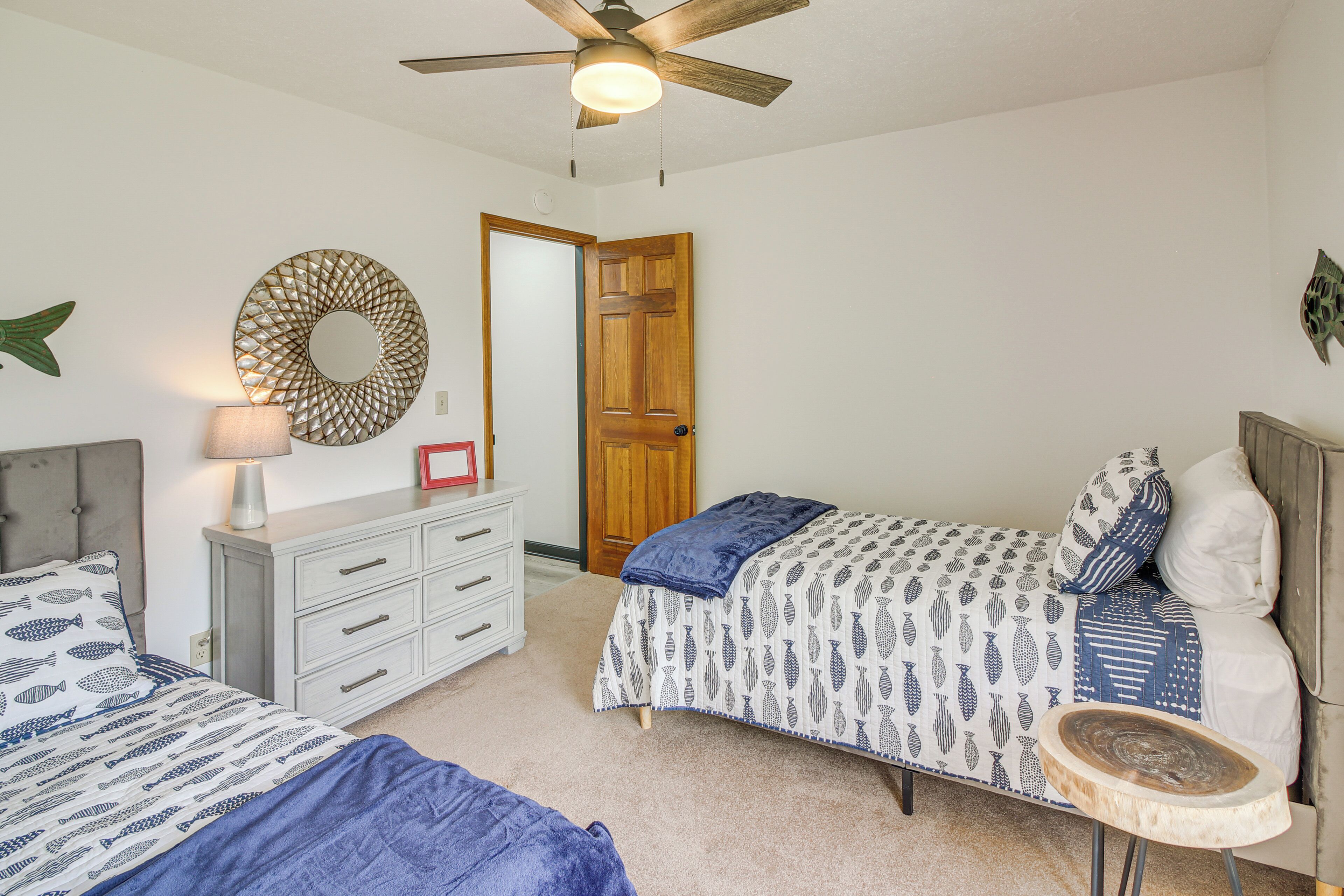 A bedroom with two beds, a ceiling fan, a wooden door, and a dresser.