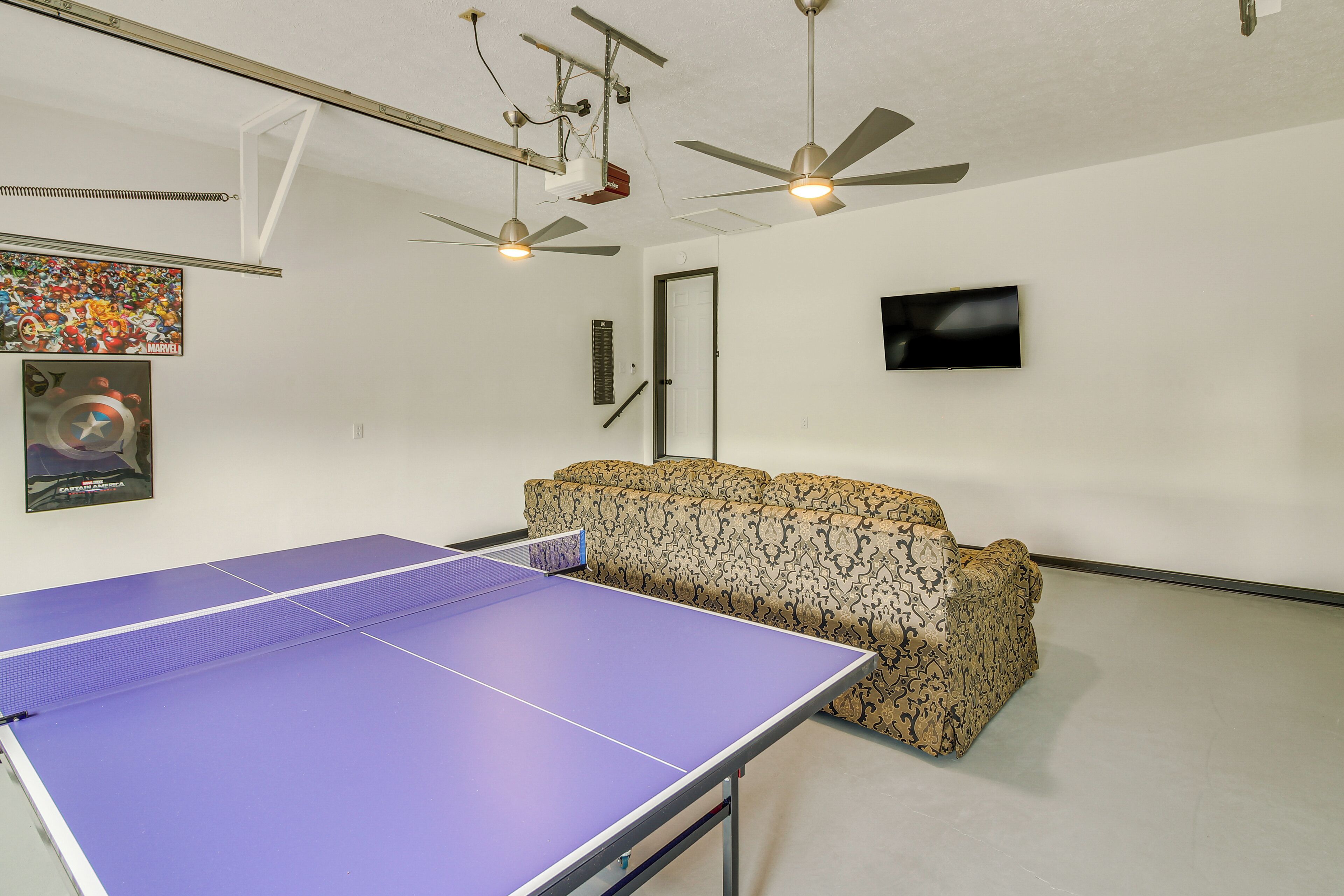 Une pièce équipée d’une table de ping-pong, de ventilateurs de plafond, d’un canapé et de décorations murales.