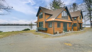 Eine zweistöckige Holzhütte mit großen Fenstern und einem geneigten Dach, gelegen am See.