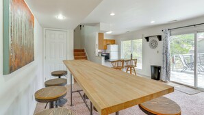 A modern kitchen with wooden cabinets, a central island, and a dining area with a long table and stools. - Balcony & Fire Pit: Home on Lake of Ozarks! (Roach)