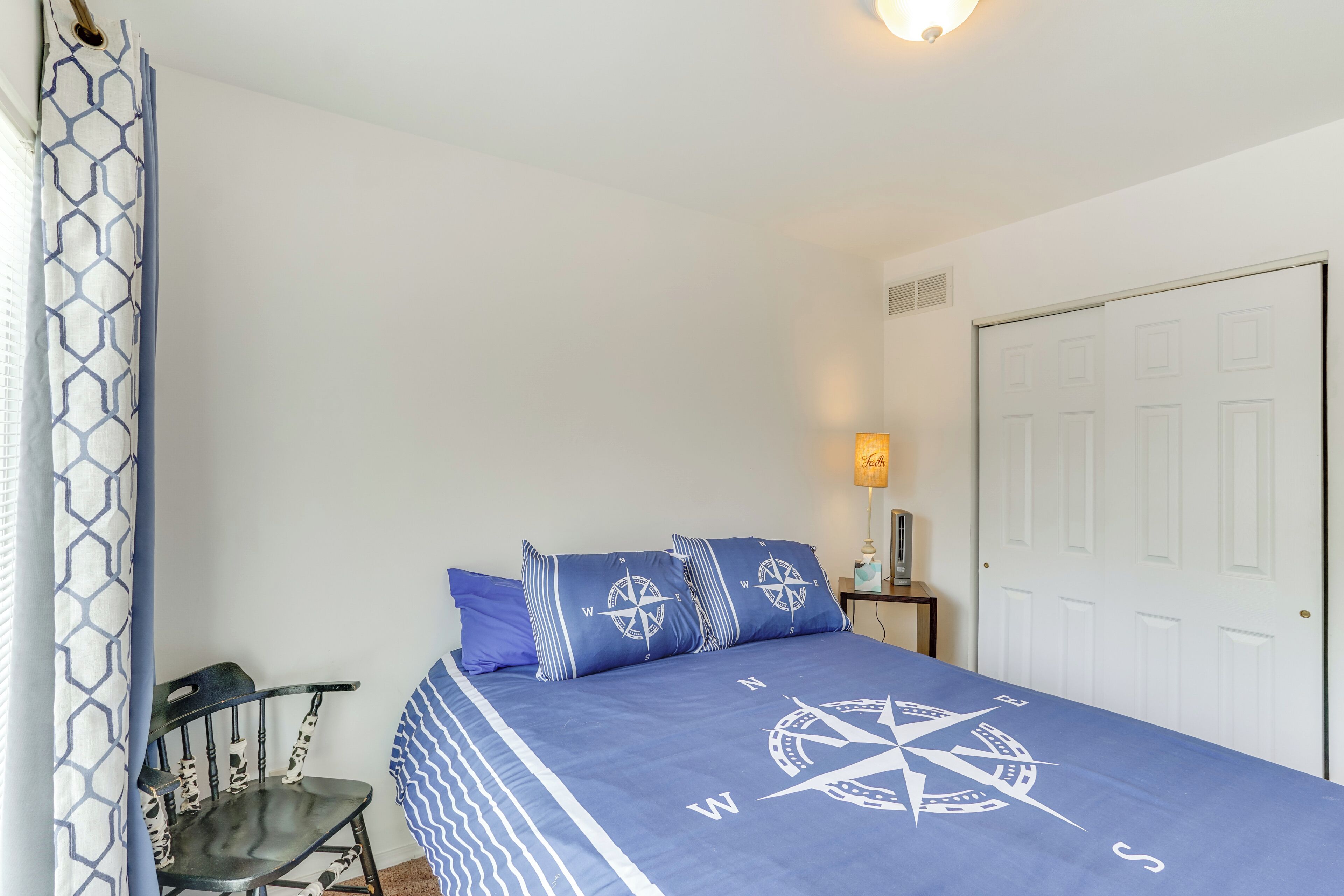 A bedroom with a bed, a chair, a nightstand, and a door.