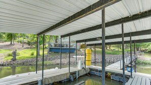 A covered dock area with a concrete platform, metal railings, and a water body. - Balcony & Fire Pit: Home on Lake of Ozarks! (Roach)