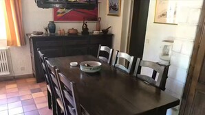 Ein Essbereich mit Holztisch und Stühlen, einem Fliesenboden und einer Küche im Hintergrund.