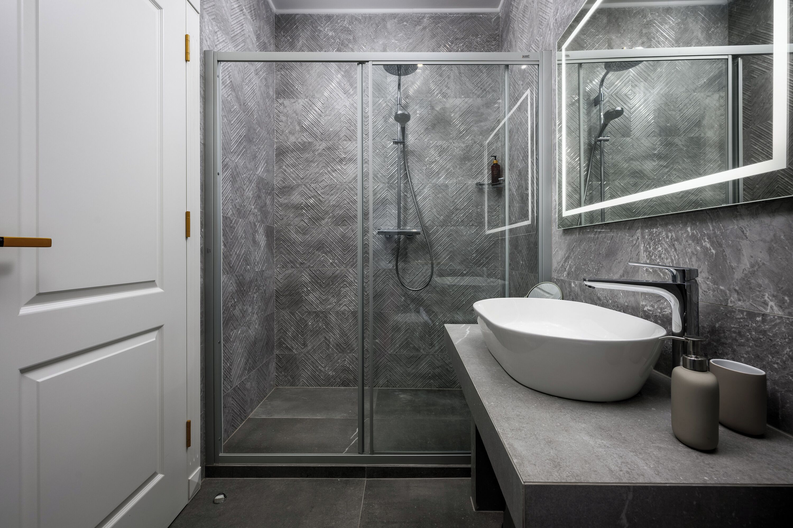 A modern bathroom with a glass-enclosed shower, a white sink, and a marble-tiled shower wall.