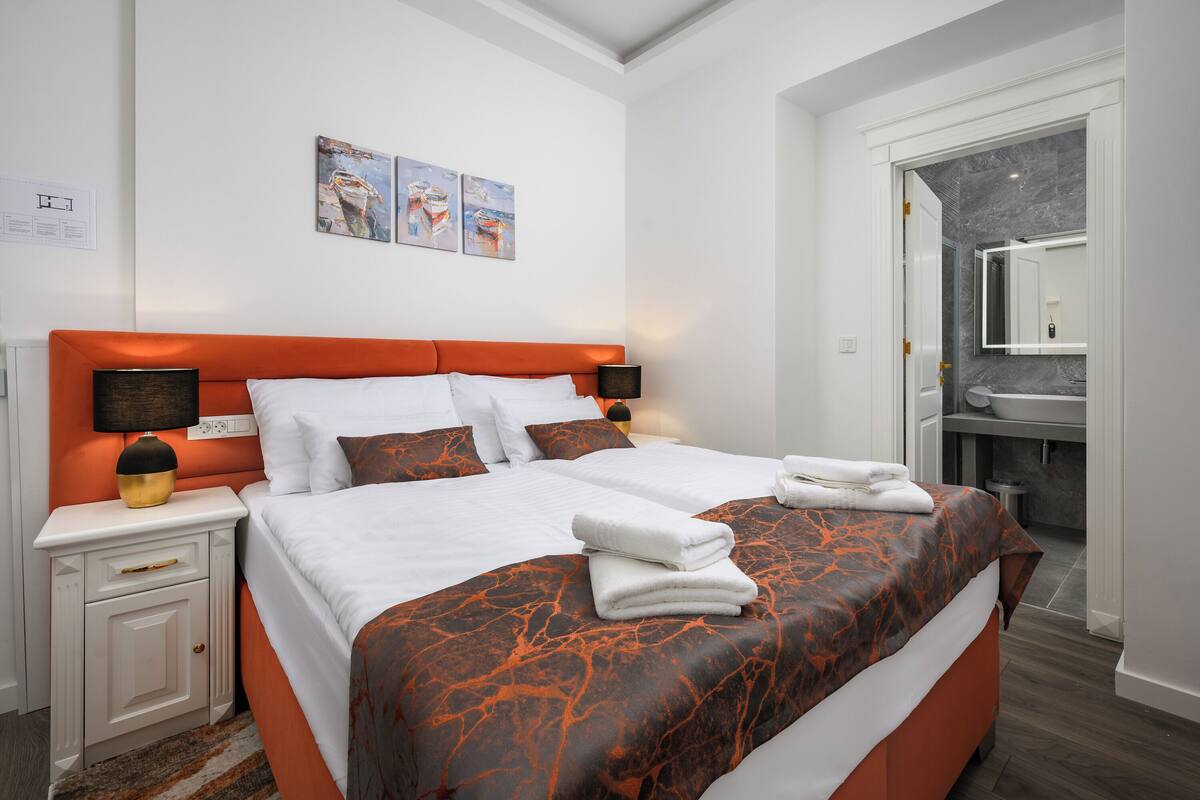 A modern hotel room with a large bed, a nightstand, a bedside table, and a bathroom visible through an open door.