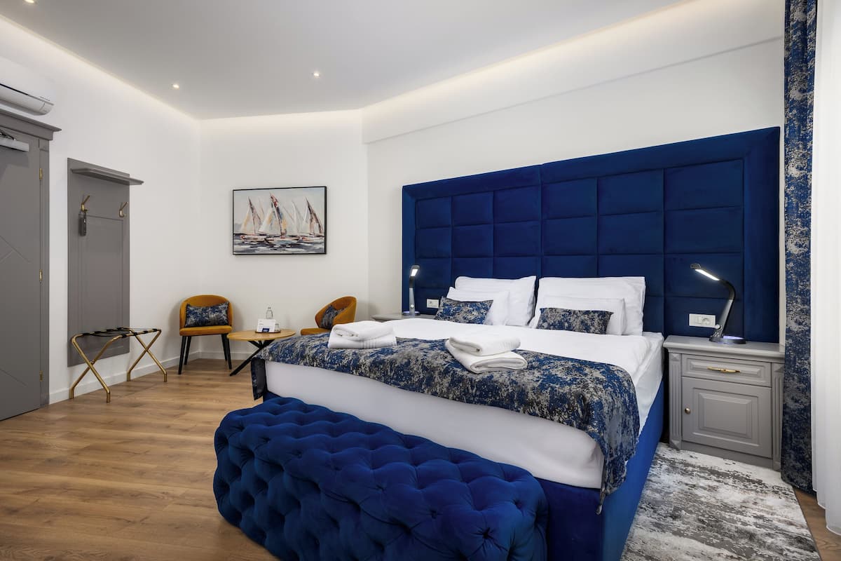 A modern bedroom with a large bed, a tufted headboard, a bedside table with a lamp, and a small seating area with a chair and table.