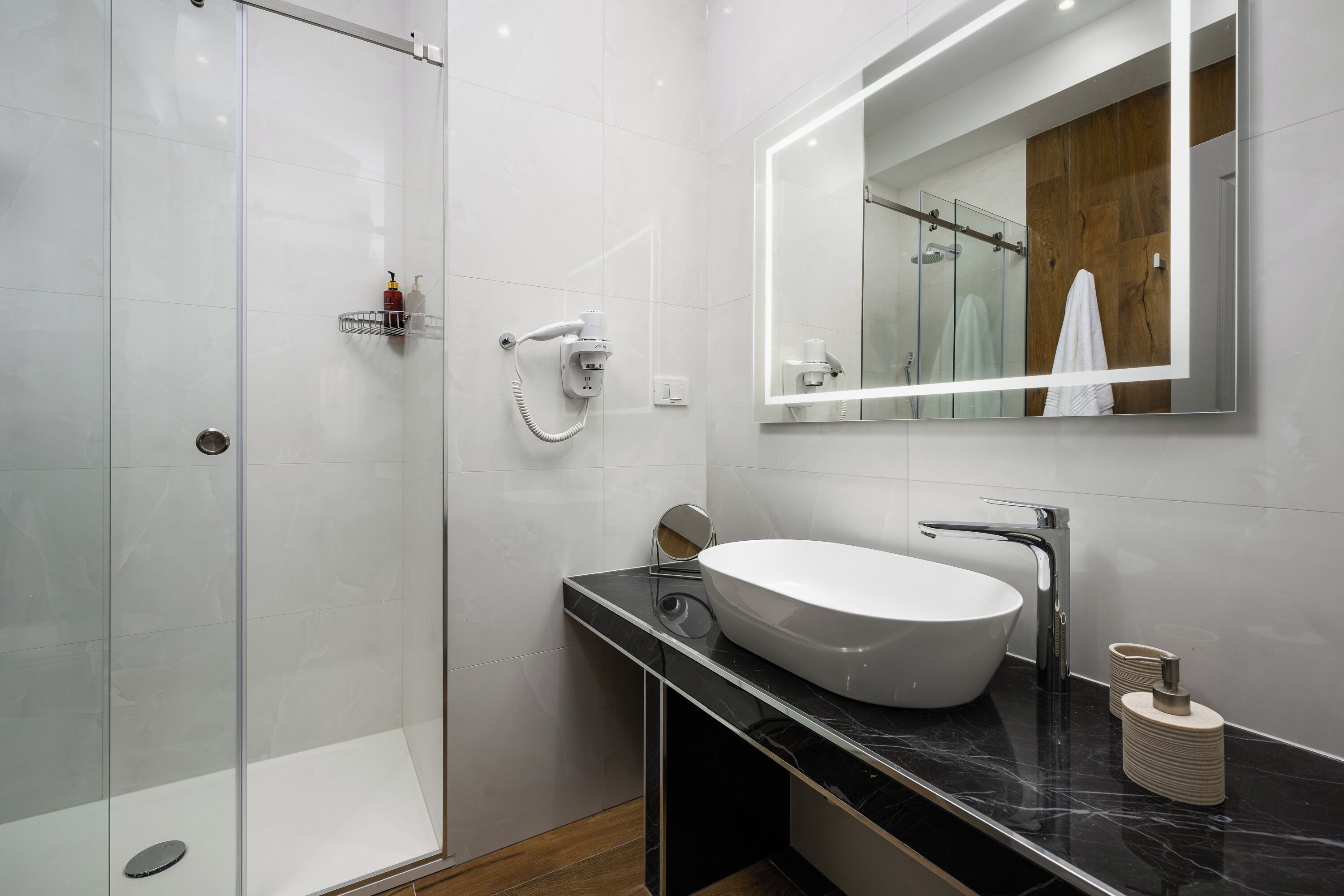 A modern bathroom with a glass-enclosed shower, a white sink, and a large mirror.