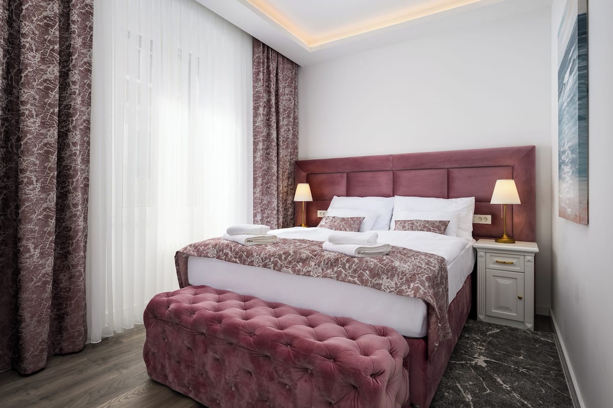 A hotel room with a large bed, two bedside lamps, a marble-patterned headboard, and a marble-patterned floor.