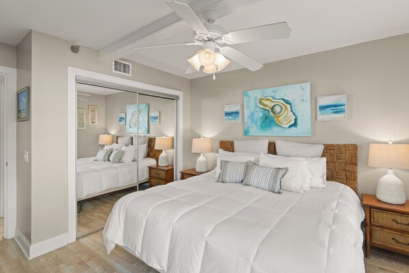 A bedroom with a large bed, a ceiling fan, and artwork on the walls.