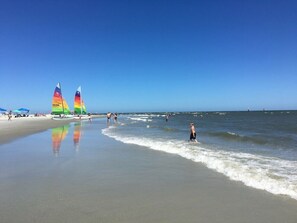 A beach with clear skies, a sandy shore, and a few people and sailboats.