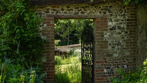 A rustic brick structure with a metal gate, surrounded by lush greenery.