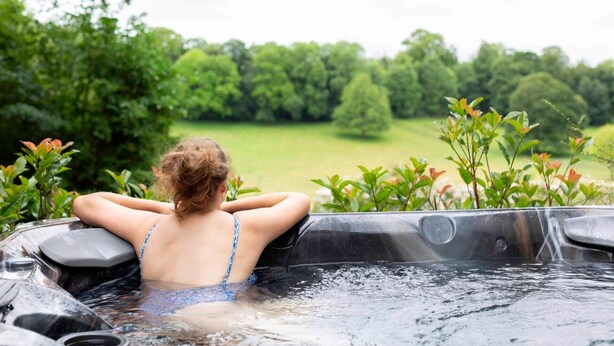 A person relaxing in a hot tub with a view of a green landscape.