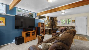 A living room with a large flat-screen TV, wooden entertainment unit, brown leather sofa, stone wall, and a door. - Frisco Mountain Retreat- Private Hot Tub (Frisco)