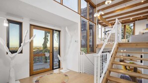Un intérieur moderne avec un escalier en bois, de grandes fenêtres et une vue sur l’extérieur.