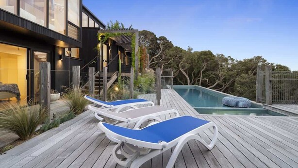 Une maison moderne dotée d’une piscine, d’une terrasse en bois et de chaises longues.