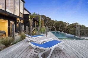 A modern house with a pool, wooden deck, and lounge chairs. - Oasis (Sorrento)