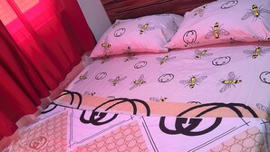 A bed with a pink and white duvet featuring a bee pattern, a Gucci branded pillow, and a Gucci branded blanket.