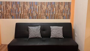 A black sofa with two patterned pillows, a wooden floor, and a wall with a geometric wood panel design and four hexagonal wall art pieces.