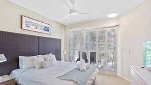 A hotel room with a large bed, a ceiling fan, a TV, and a window with blinds.