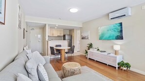 A modern living room with a grey sofa, a round dining table, and a kitchen in the background.
