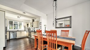 A modern kitchen with wooden cabinets, a dining table with chairs, and a large window.