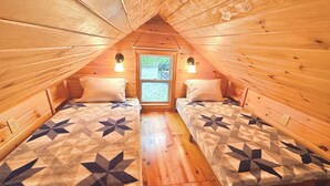 A cozy attic bedroom with two beds, wooden walls, and a window.