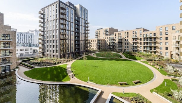 A modern residential building complex with multiple apartment buildings, a central green lawn, and a small water feature.