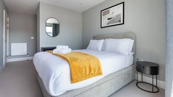 A modern hotel room with a large bed, a round mirror, a framed abstract painting, and a small bedside table.