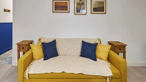 A yellow sofa with a white quilt, two blue pillows, and two wooden nightstands with drawers.