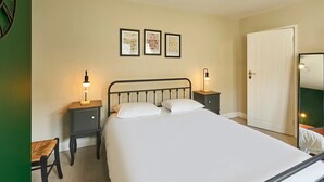 A bedroom with a bed, two bedside tables with lamps, a chair, a door, and three framed pictures on the wall.