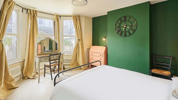 A room with a bed, a desk with a chair, a dresser, and a wall clock.