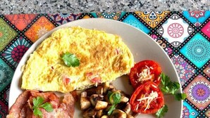 Ein Teller mit Omelett, Tomatenscheiben, Pilzen und Würstchen.