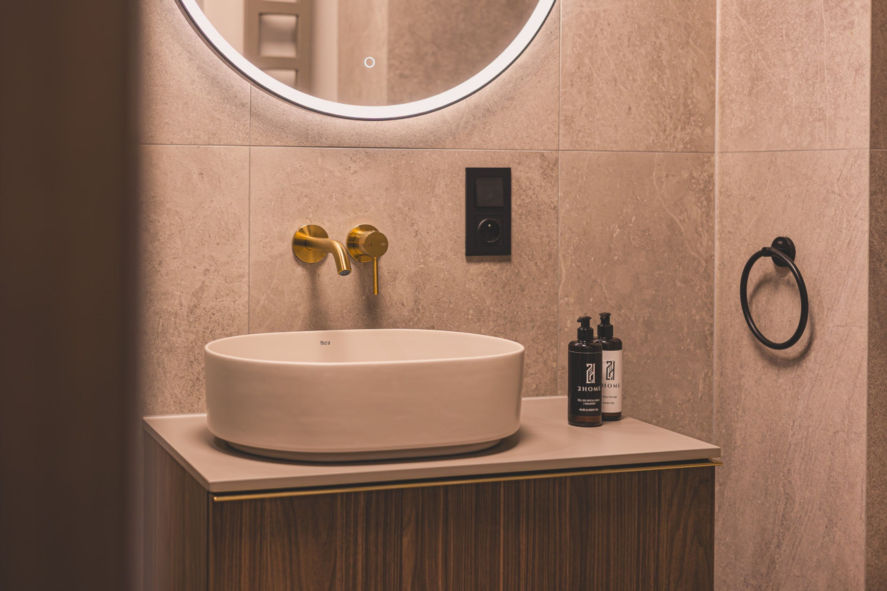 A bathroom with a round sink, gold faucets, a mirror, and a towel ring.