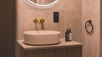 A bathroom with a round sink, gold faucets, a mirror, and a towel ring.