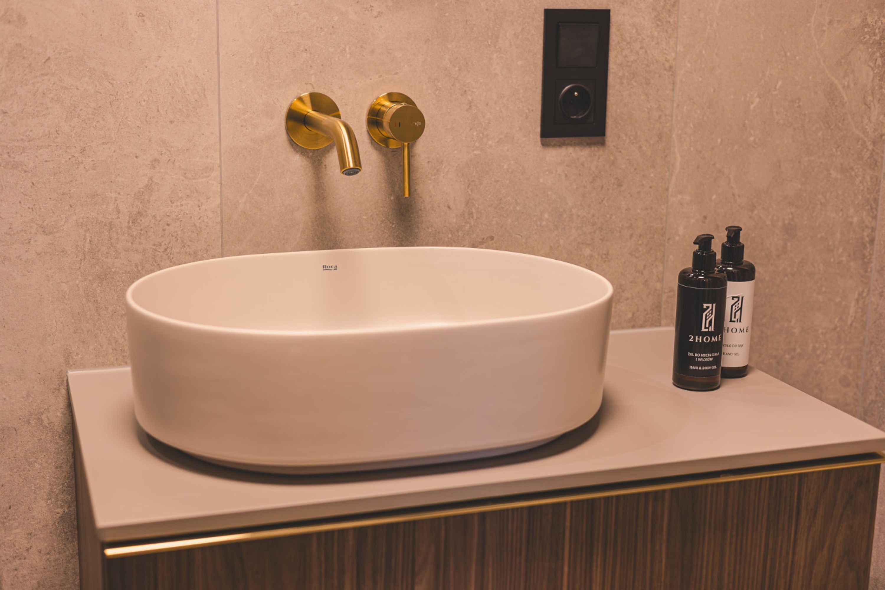 A bathroom with a white sink, gold faucets, and two black bottles on the counter.