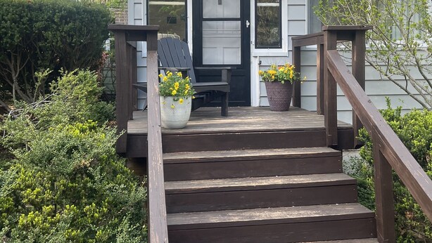 Ein kleines Haus mit einer Veranda, einer Haustür und einer Treppe, die zum Eingang führt.