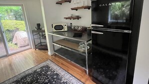 Eine moderne Küche mit einem schwarzen Kühlschrank, einer Mikrowelle und einer Kaffeemaschine auf der Arbeitsplatte. Darüber befinden sich Regale mit Gläsern und einem Korb.