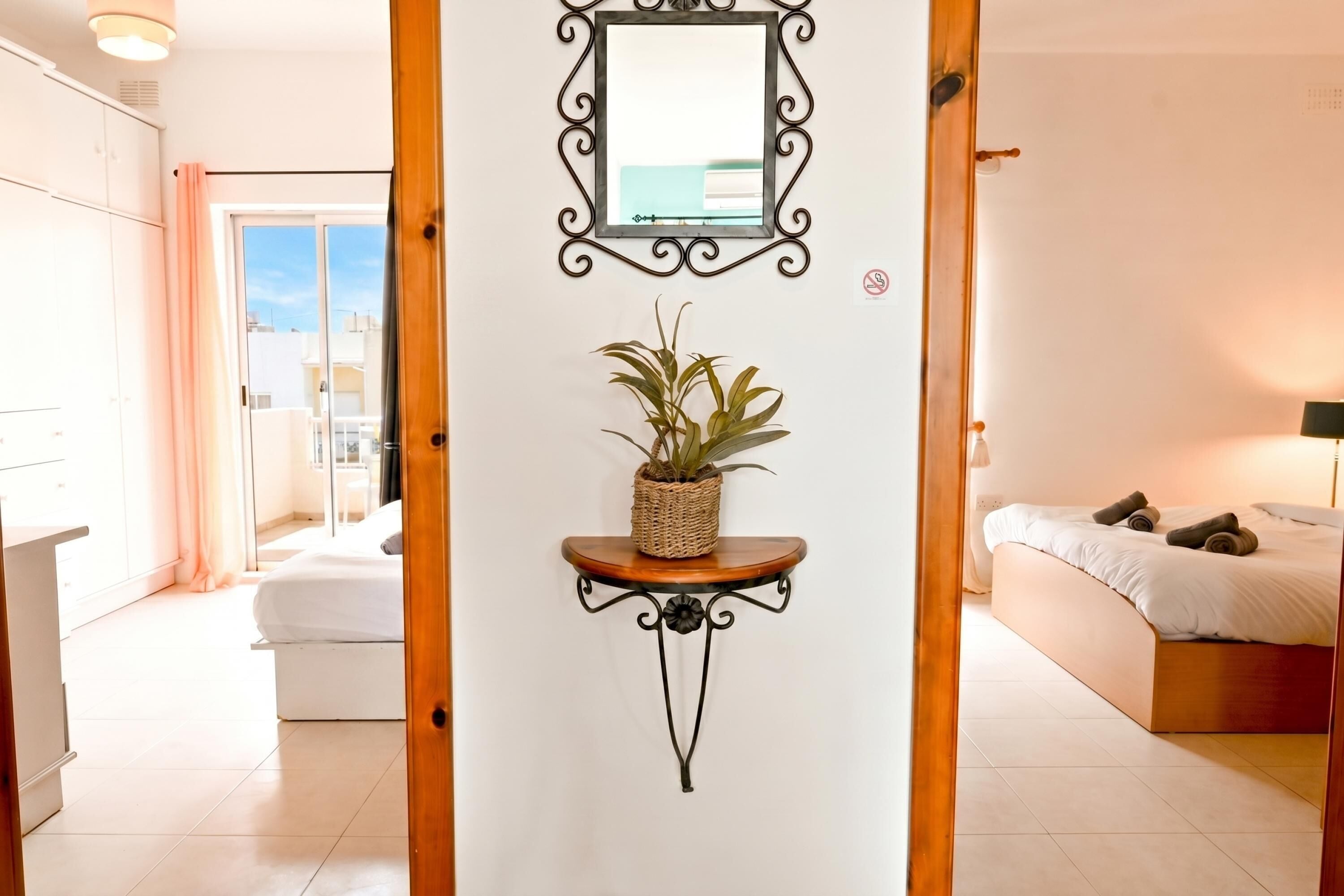 A bedroom with a bed, a bedside table with a plant, a mirror, and a view of the outside.