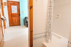 A bathroom with a white bathtub, a shower area, and a door with a bulletin board. - Seaview Apart 5mn From Sea Xemxija (St. Paul's Bay)
