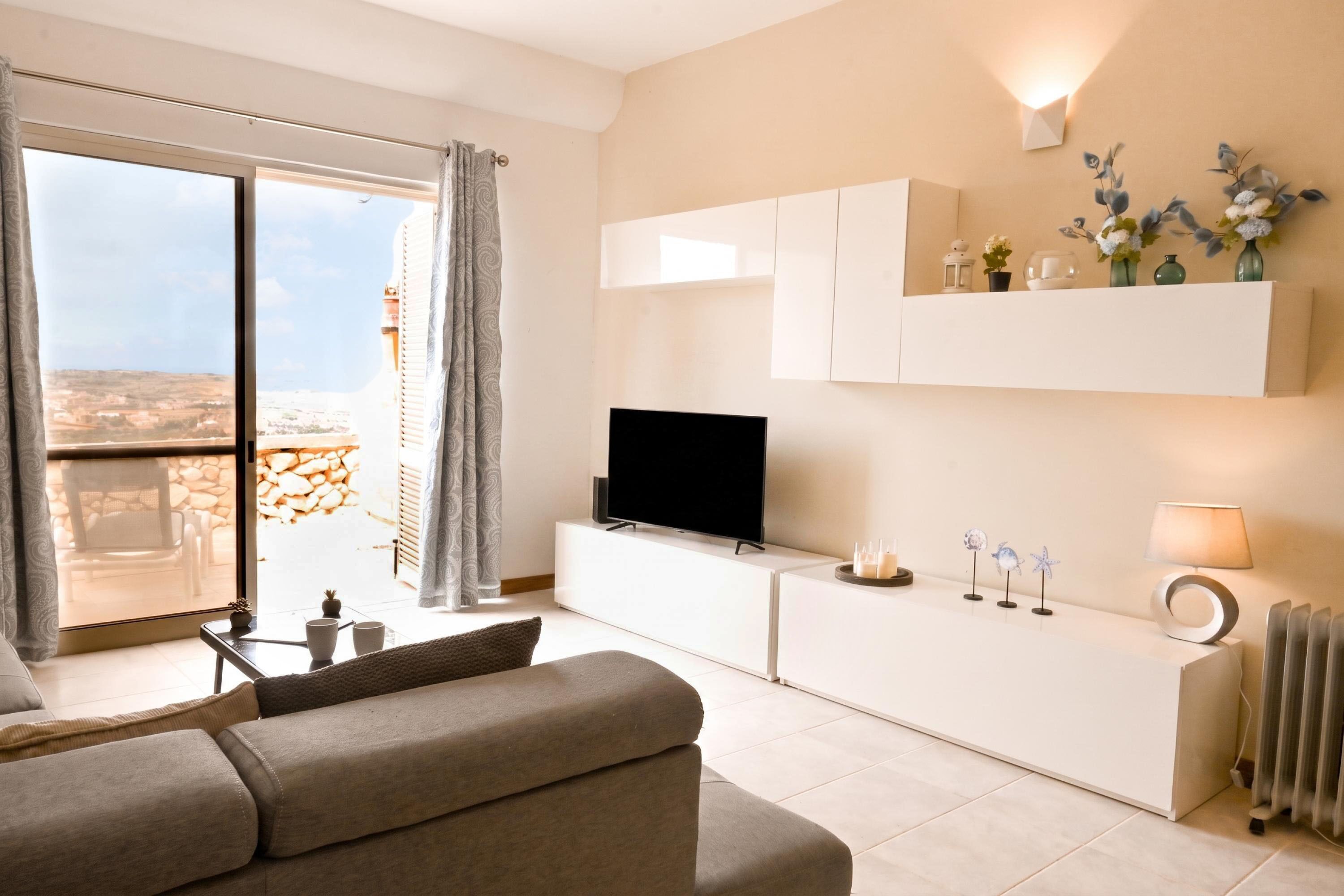 Una sala de estar moderna con un televisor de pantalla plana, un sofá, una mesa de centro y vistas al exterior.
